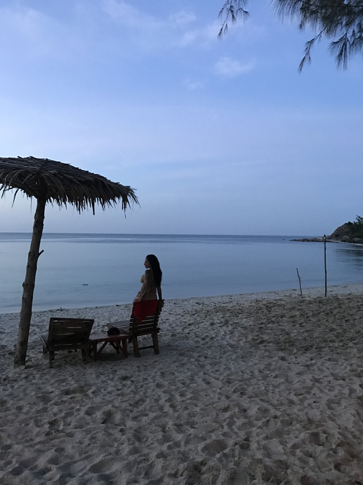 Person standing on a beach at twilight with a straw umbrella.