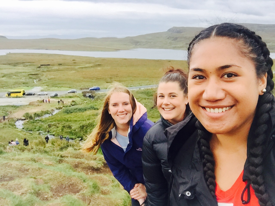 Three people smiling in a green landscape near a road.