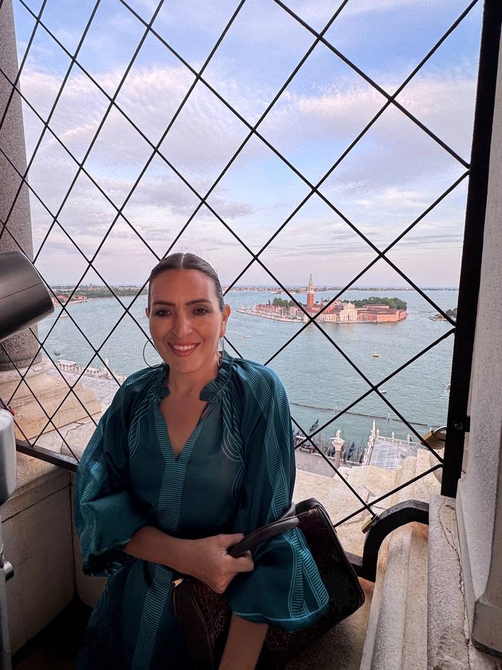Smiling woman in front of a railing with a waterway and a city in the background.
