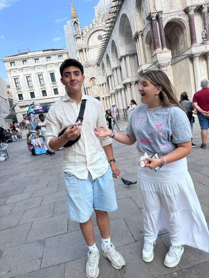 Two people standing on a street with a historic building in the background.