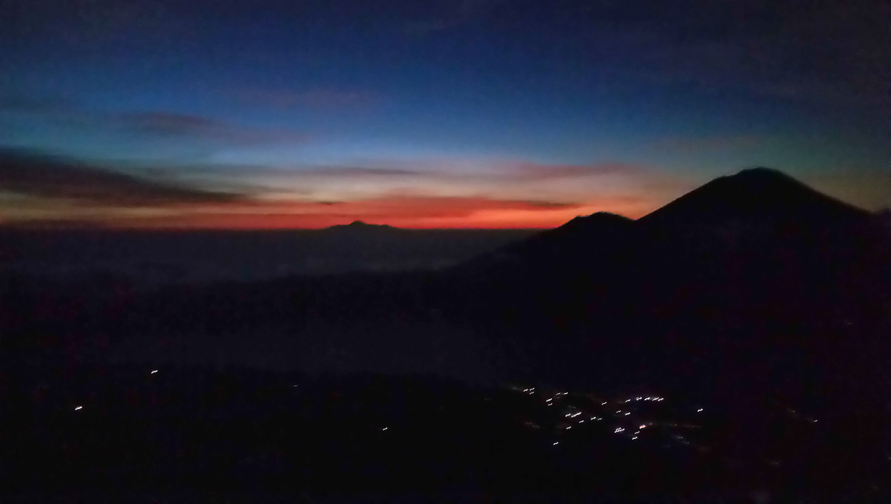 Sunset with a silhouette of mountains and lights in the distance.