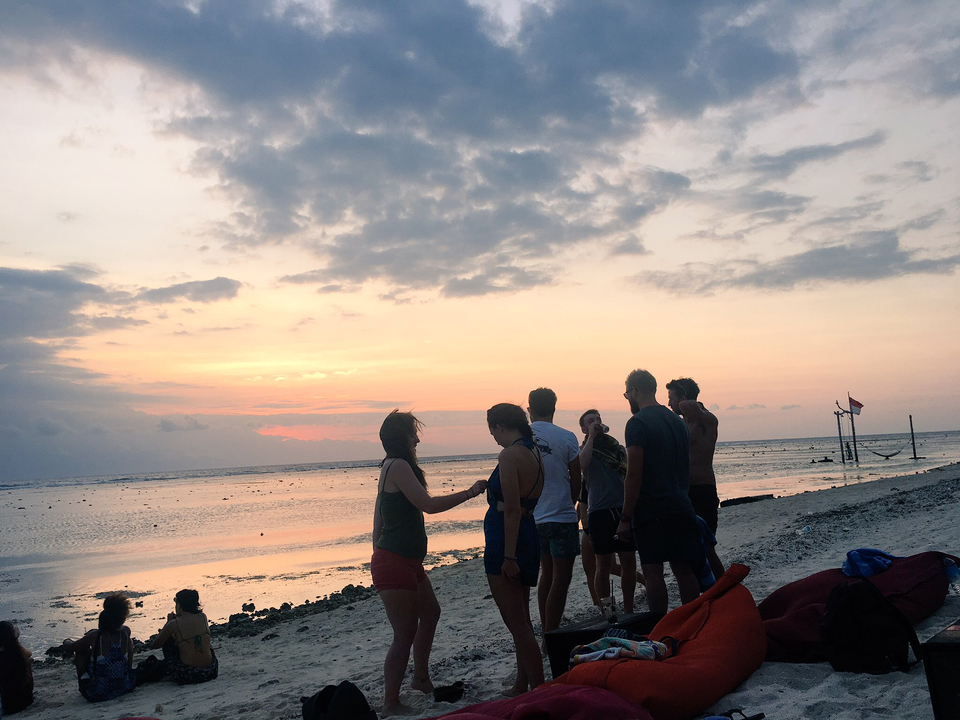 People gathered on a beach during a colorful sunset.