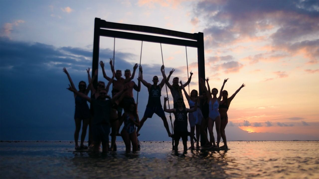Group of people posing on swings over the sea.