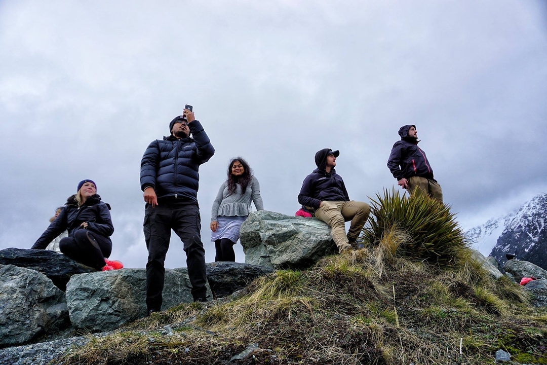 Group of people standing on rocky terrain with mountainous backdrop.