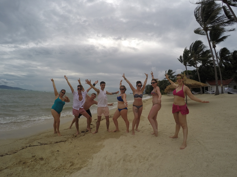 Group of people posing joyfully on a sandy beach.