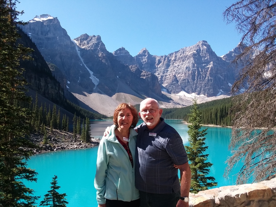 Couple souriant devant un lac turquoise et des montagnes.