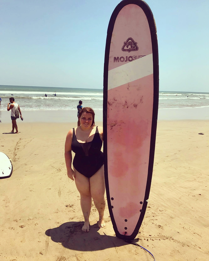 Woman standing next to a surfboard on a beach.