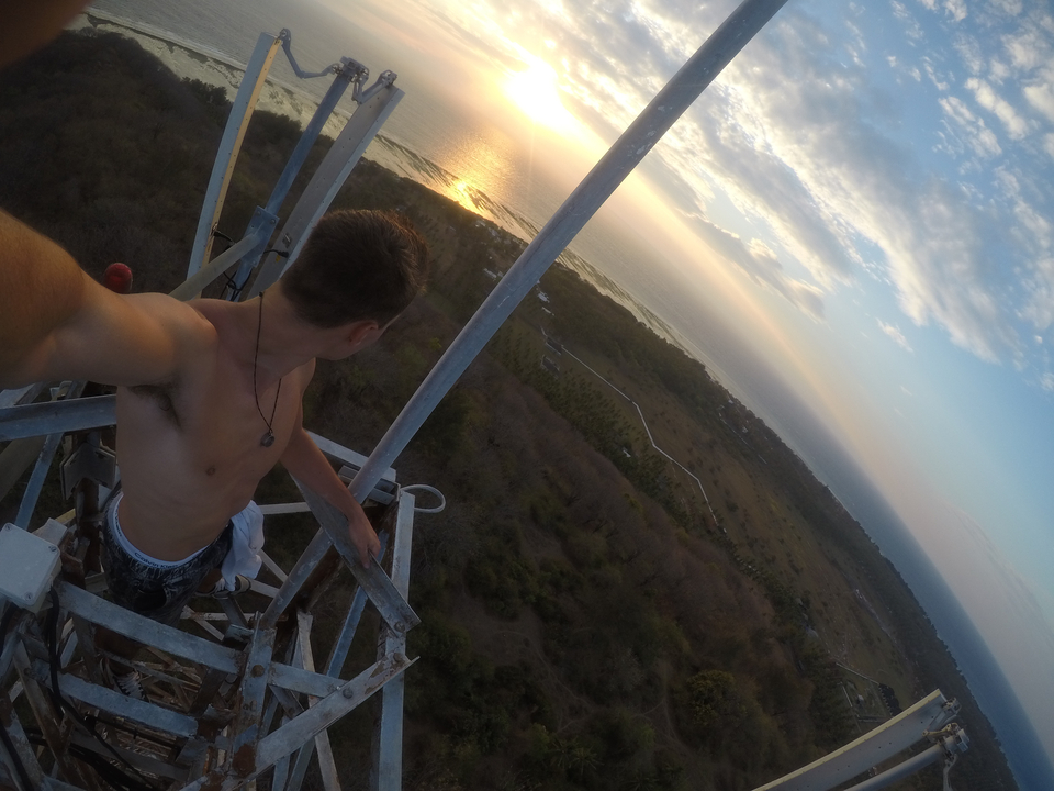 Person atop a structure overlooking a scenic coastline at sunset.