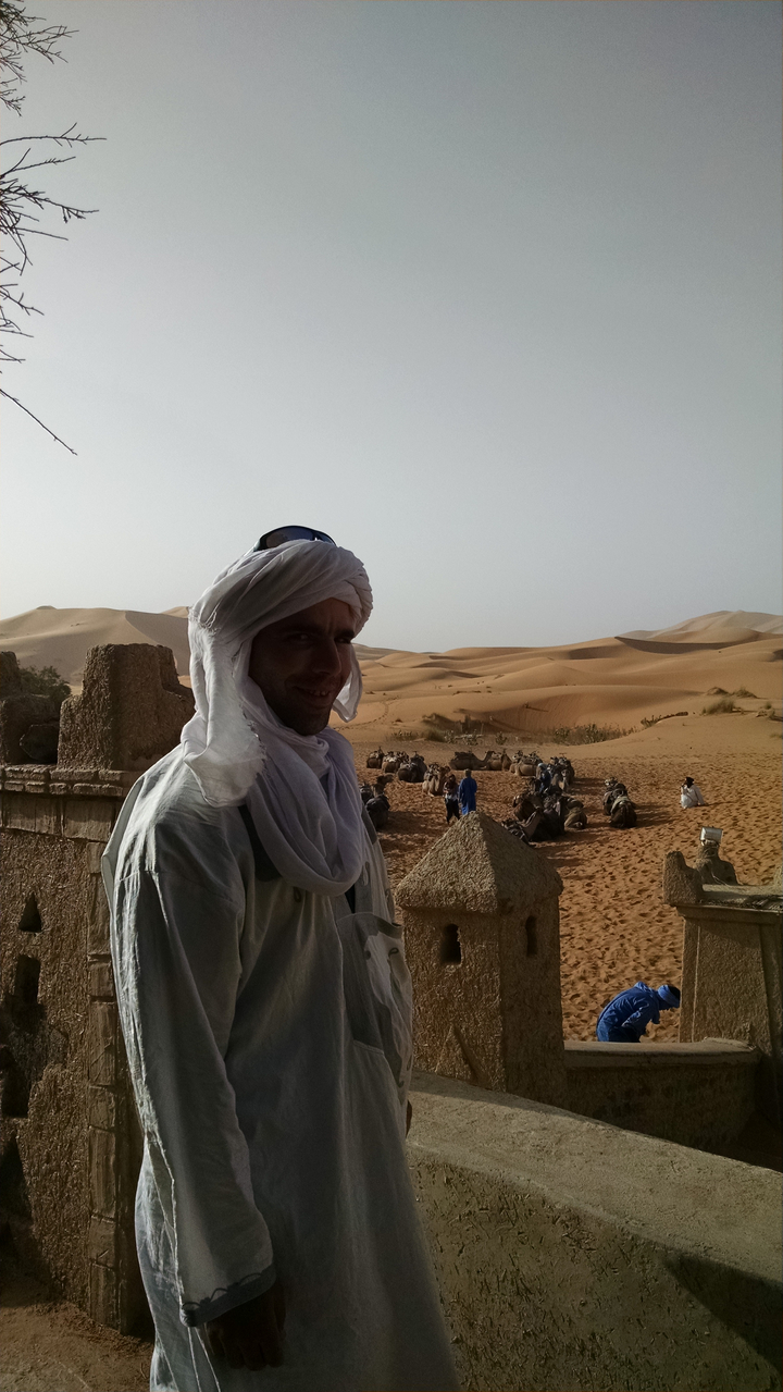 Person in traditional attire with camels in desert.