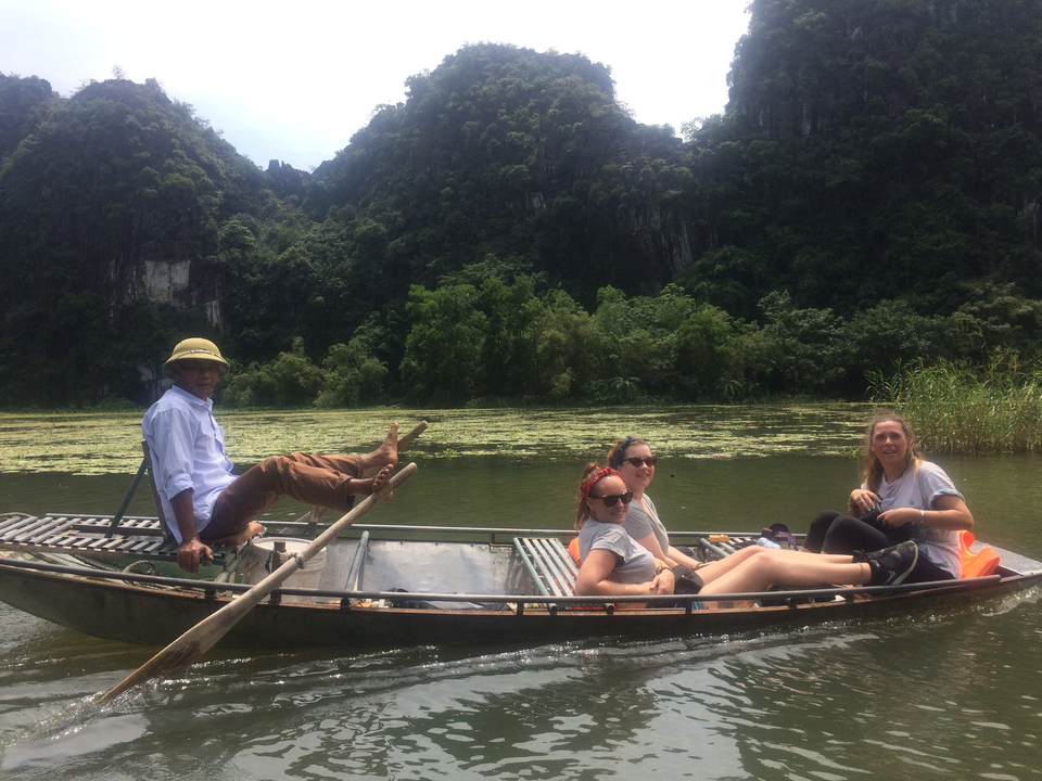 Three passengers on a rowboat in a lush, green landscape.