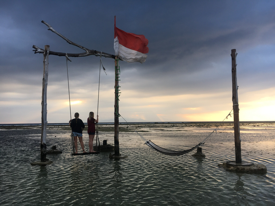 Two people on swings in shallow water during sunset.