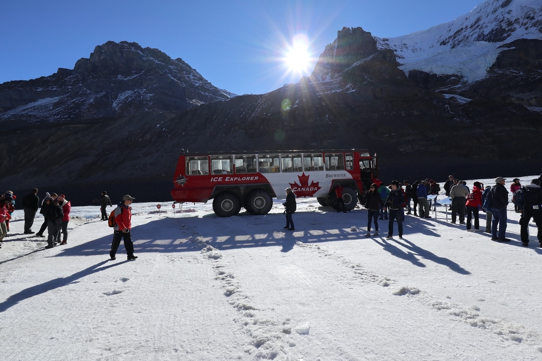 Personnes debout près d'un véhicule d'exploration des glaces rouge et blanc sur un glacier.