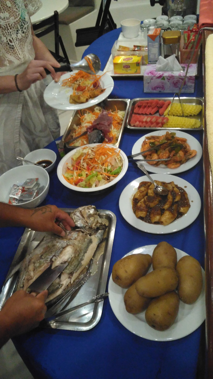 Plusieurs plats de nourriture sur une table avec une personne servant du poisson.