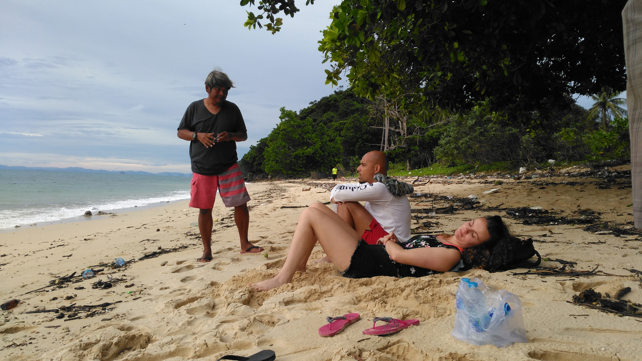 Trois personnes sur une plage de sable avec des arbres et l'océan en arrière-plan.