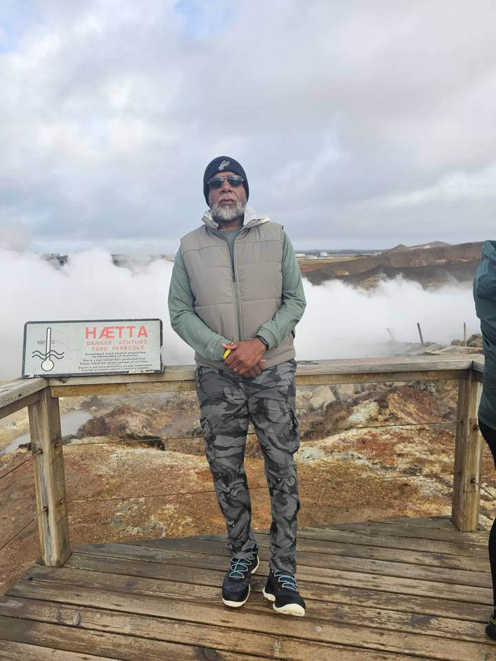 Person standing on a boardwalk near steaming ground.