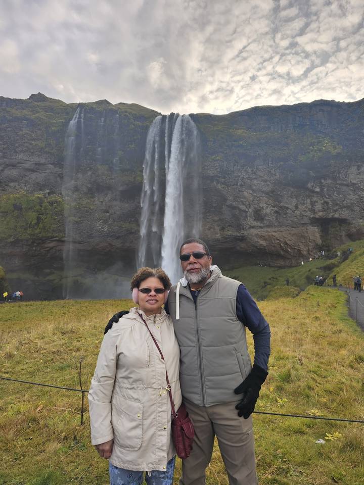 Two people posing with a waterfall in the background.