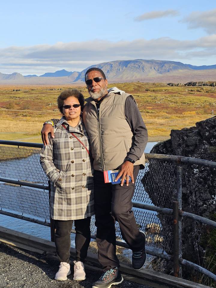 Two people standing on a bridge with landscape background.