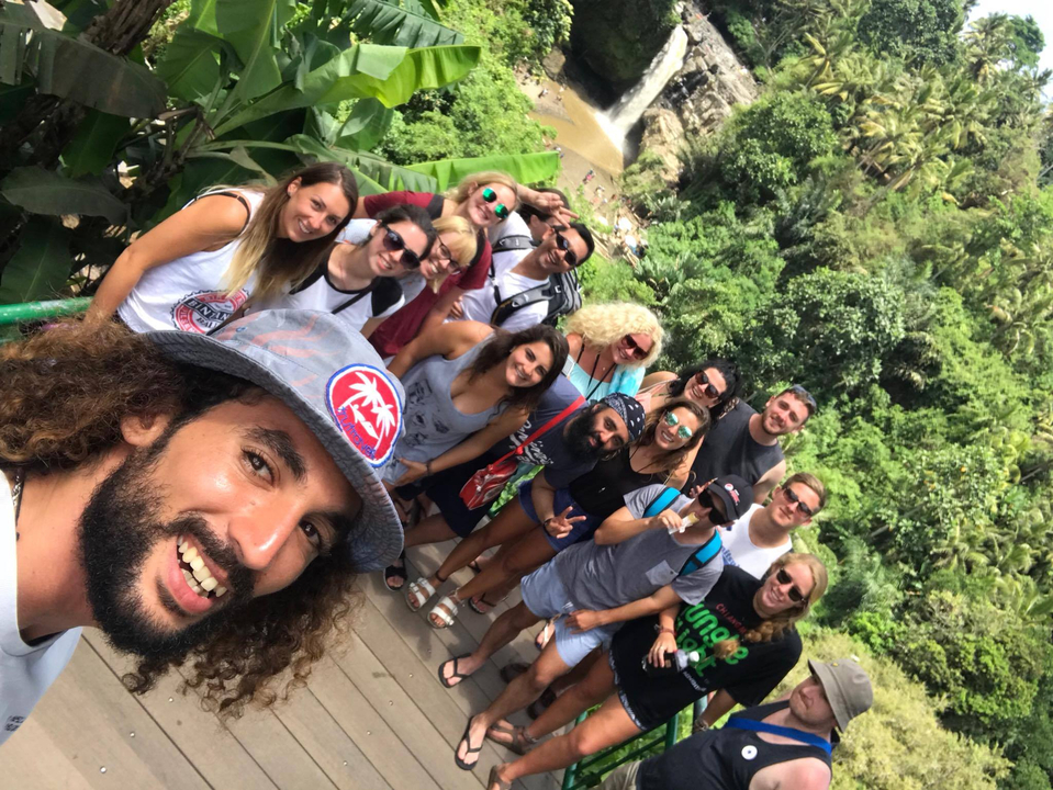 Group posing in front of a waterfall with lush greenery.