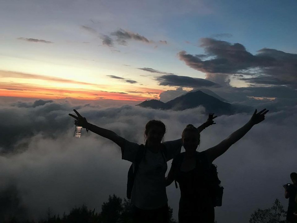 Silhouetted hikers celebrating on a mountain at sunrise.