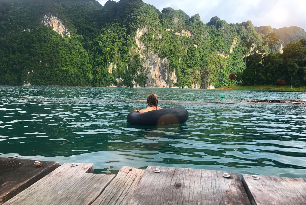 Person floating on an inner tube in a lake surrounded by cliffs.