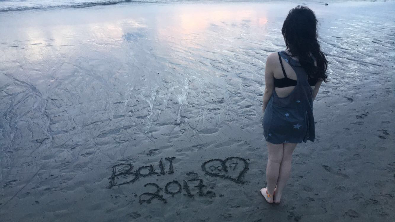 Persona de pie en la playa con arena escribiendo.