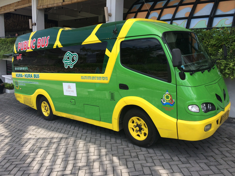 Green and yellow public shuttle bus parked on a paved lot with cartoon turtle logo.