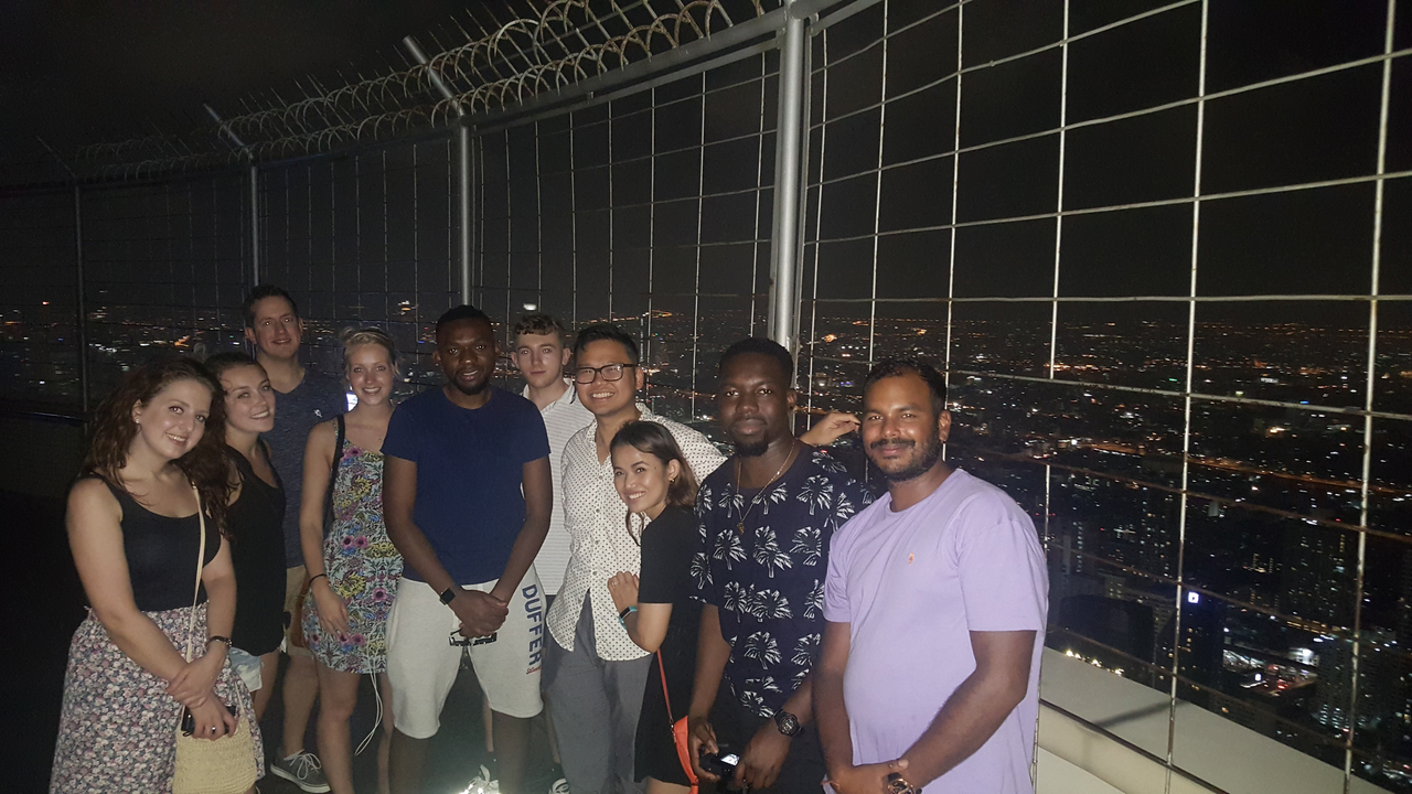 Group of people on a building rooftop with city skyline at night.