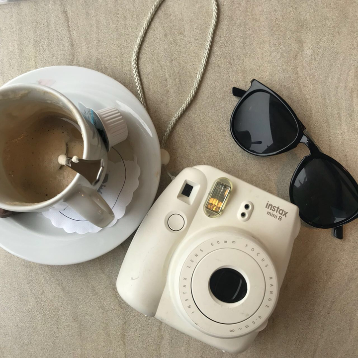 Coffee cup, camera, and sunglasses on a table.