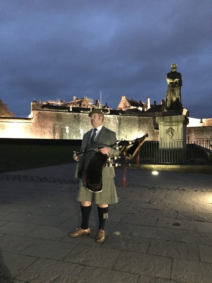 Person playing bagpipes in front of a lit building at night.