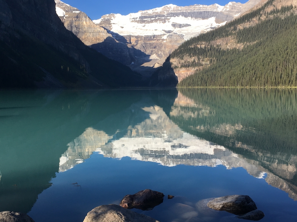 Lake reflecting snow-capped mountains under a clear sky.