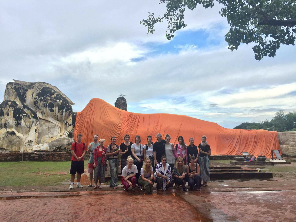 A group posing in front of a reclining Buddha statue covered in an orange cloth.