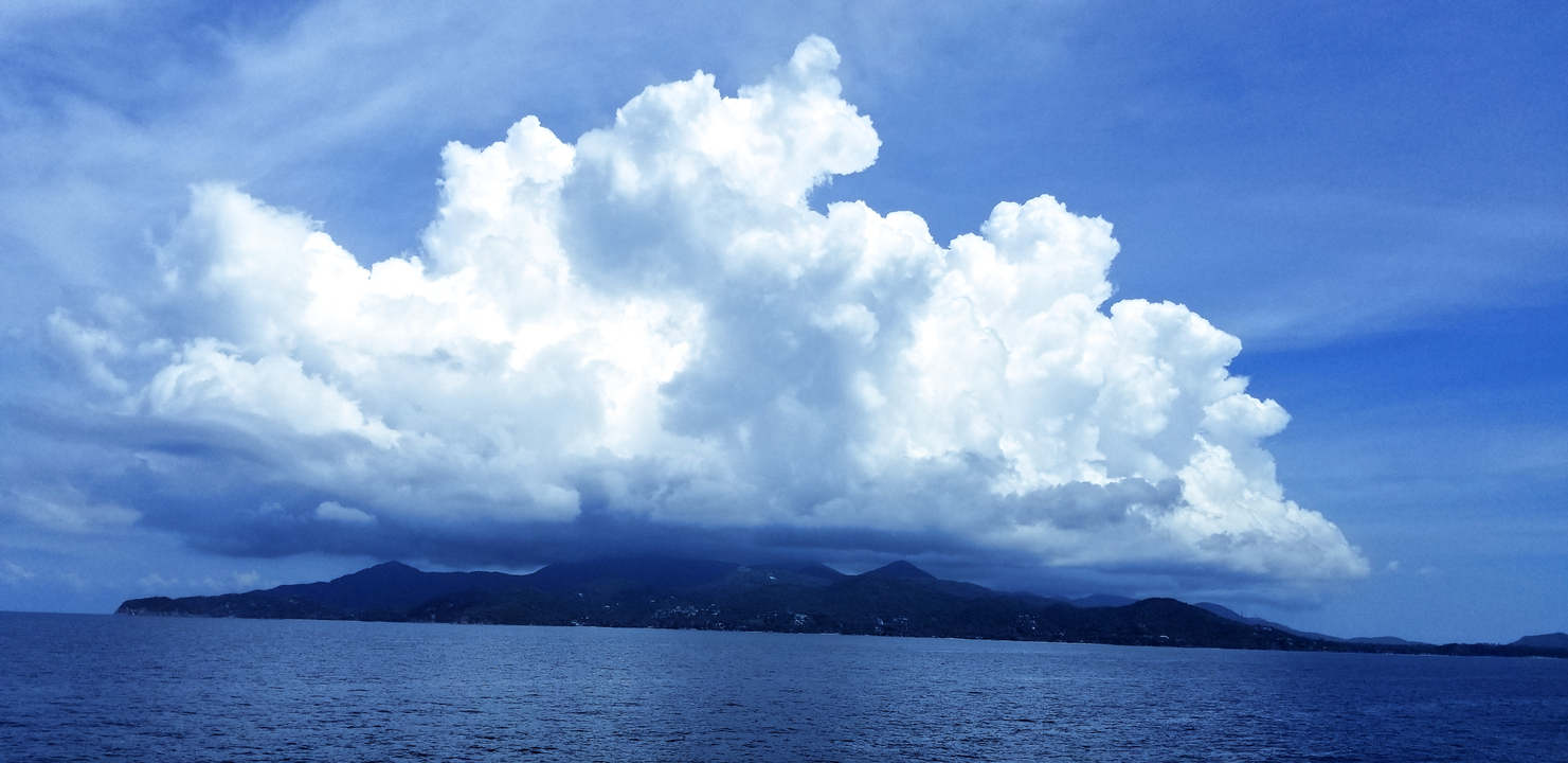 Vast ocean with dramatic cloud formations above an island.