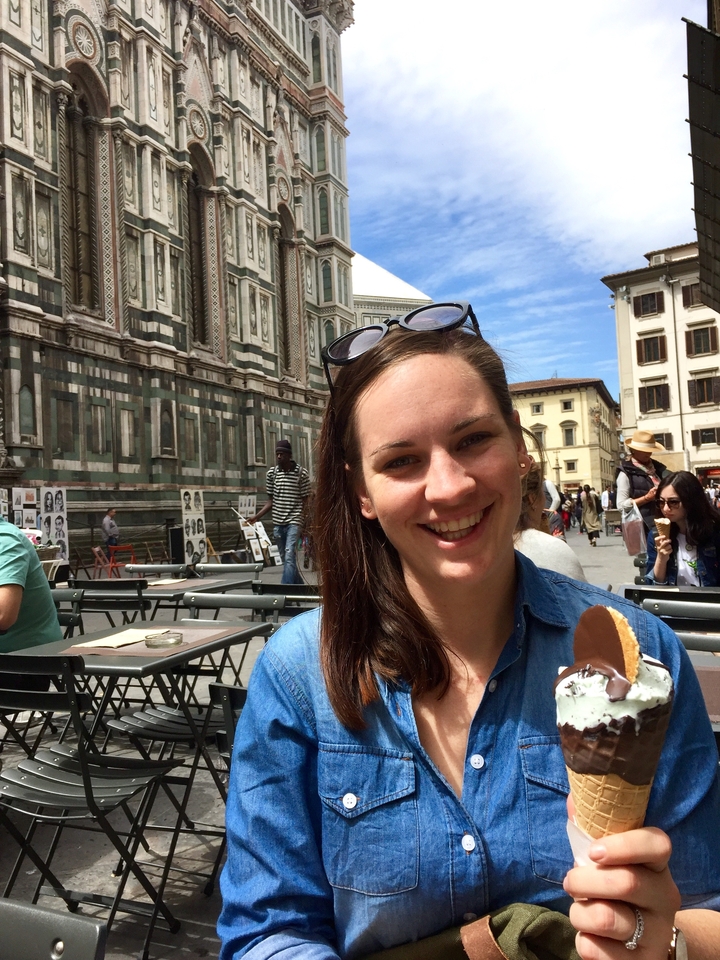 Woman enjoying ice cream at an outdoor cafe near a historical building.