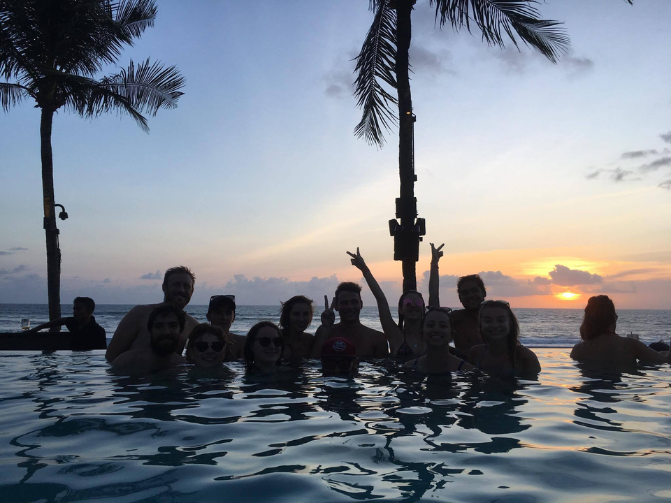 People relaxing in a pool with palm trees during sunset.