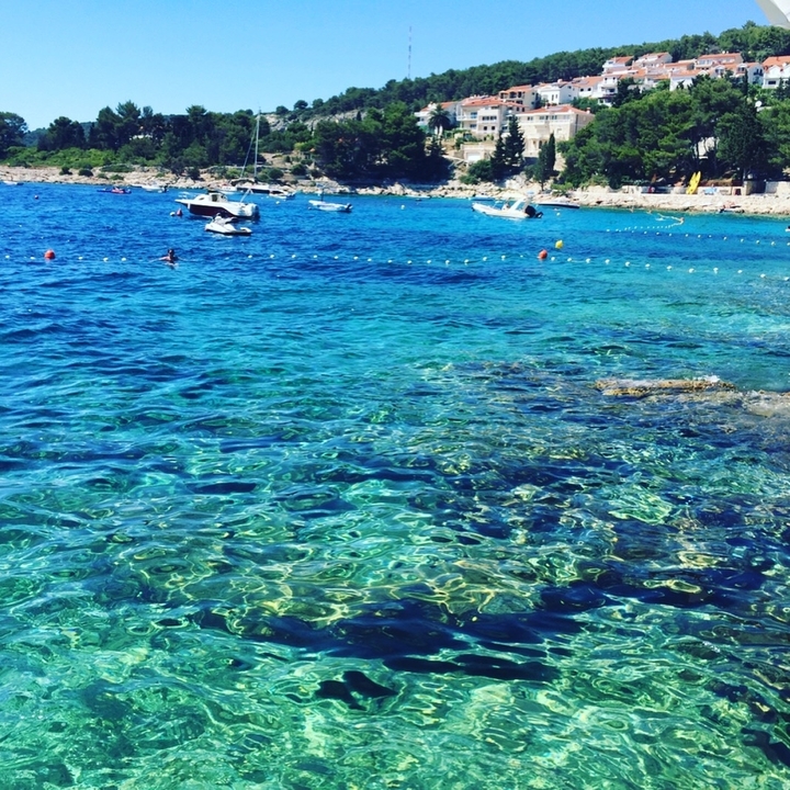 Clear blue water with boats and people swimming.