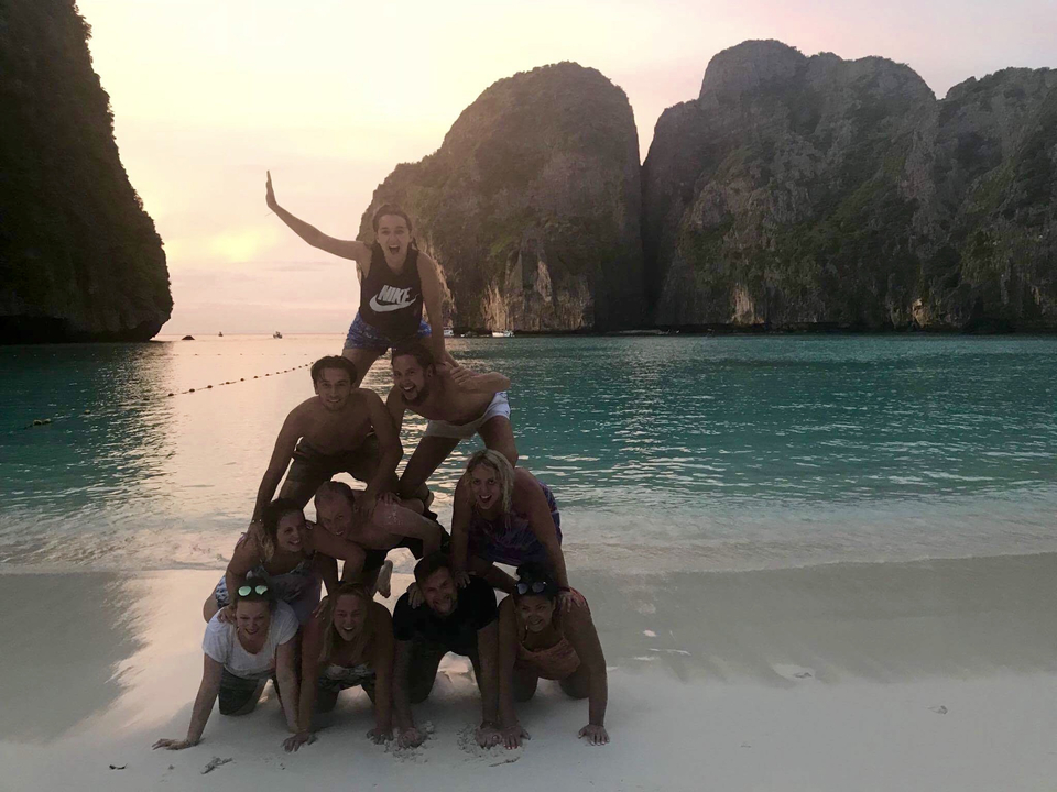 Group of people forming a human pyramid on a beach at sunset.