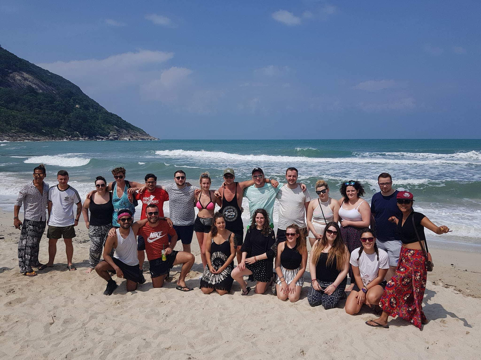 Group photo of people on a beach with the sea in the background.