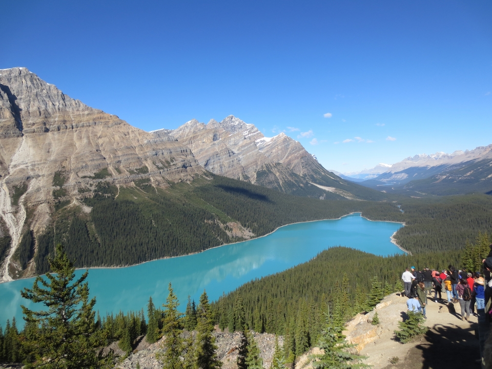 Lac turquoise entouré de montagnes, avec des personnes observant depuis un point de vue.