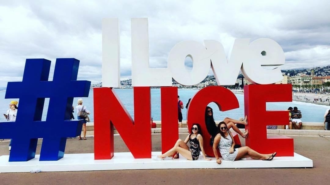 Group of people posing with a large 'I Love Nice' sign by the waterfront.