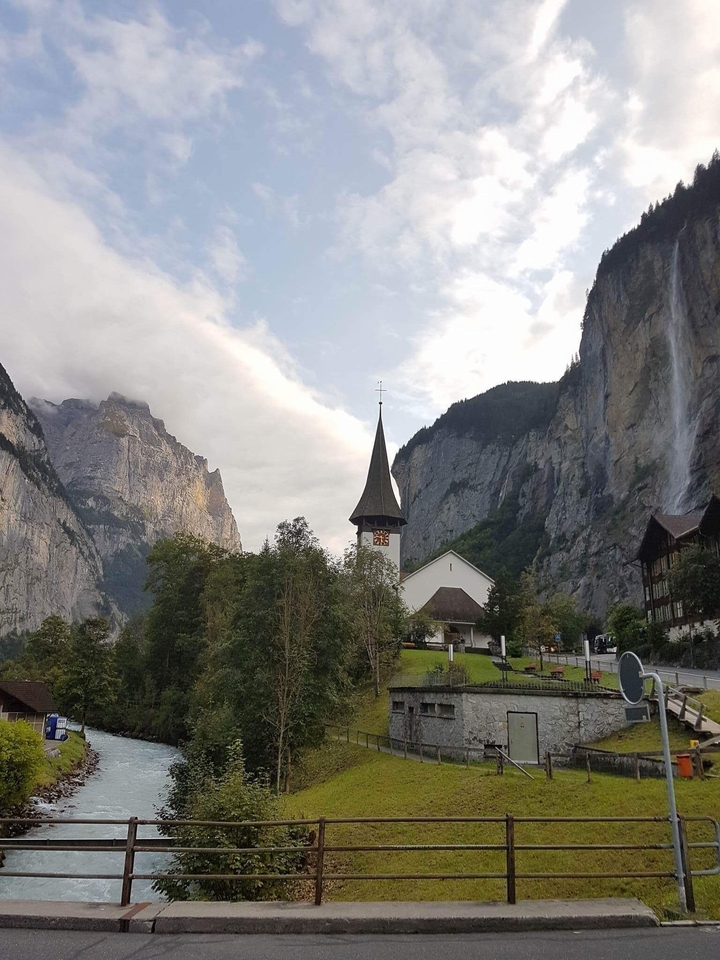 Charming village landscape with church steeple and waterfall in mountainous valley.