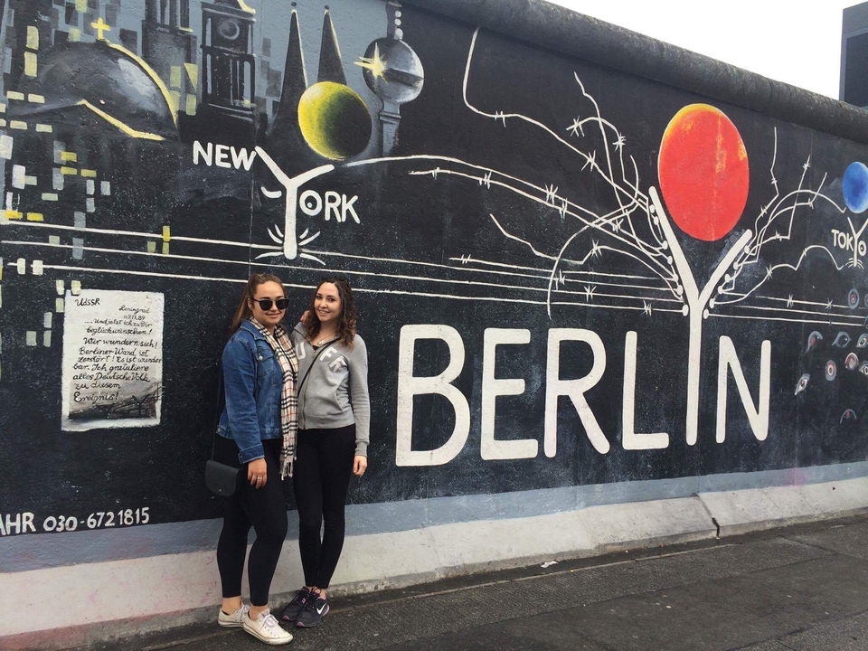 Two people standing in front of a Berlin wall mural.