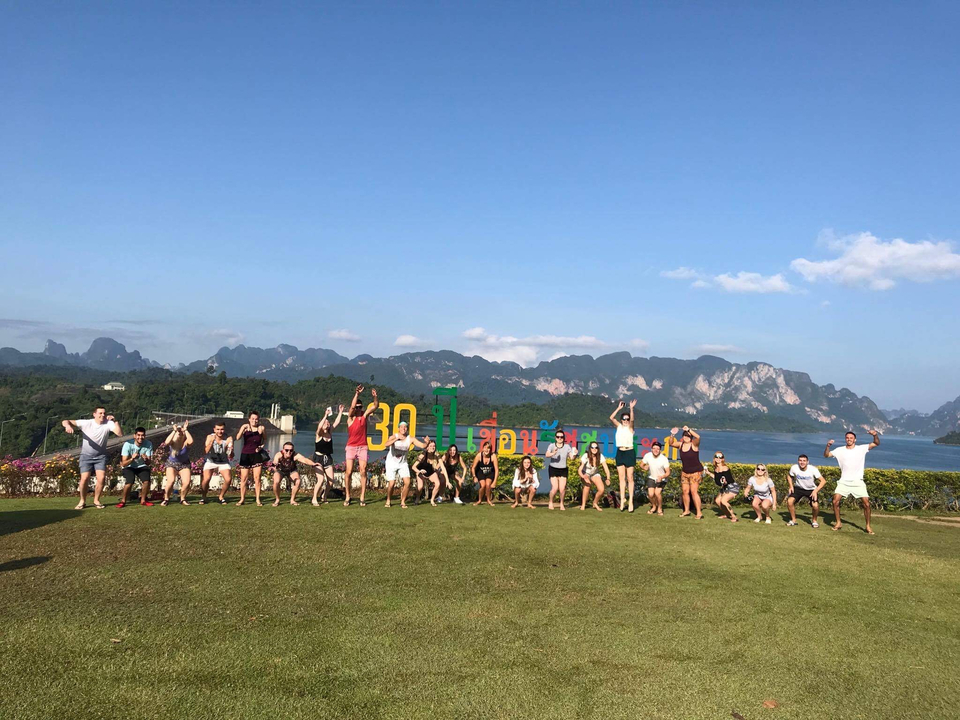 Group posing energetically in a field with hills.
