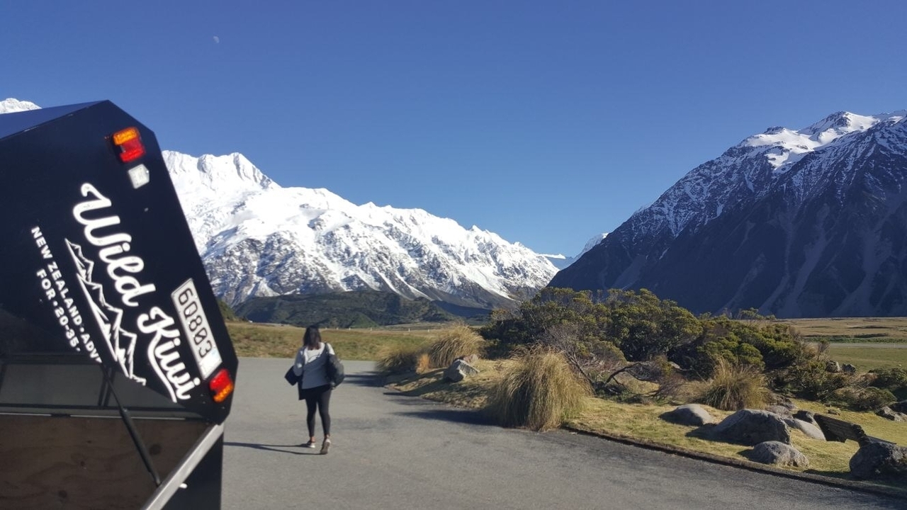 Person walking towards snow-capped mountains with a camper van on the road.