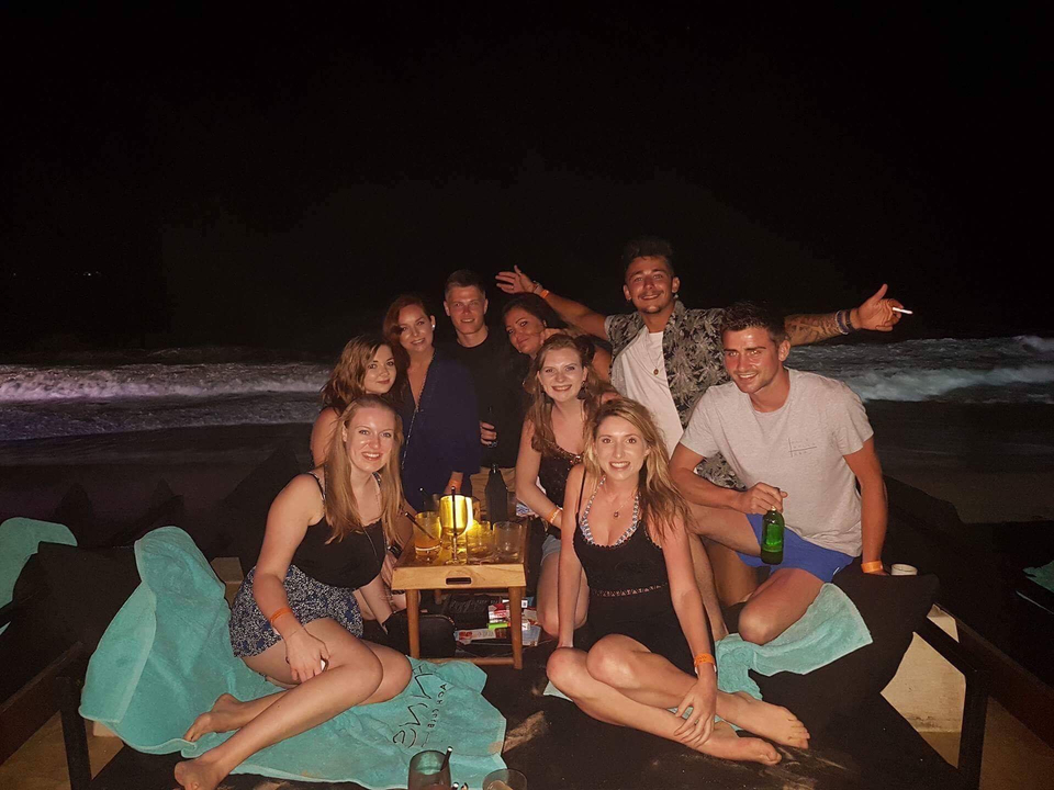 Group sitting on a beach at night with drinks.