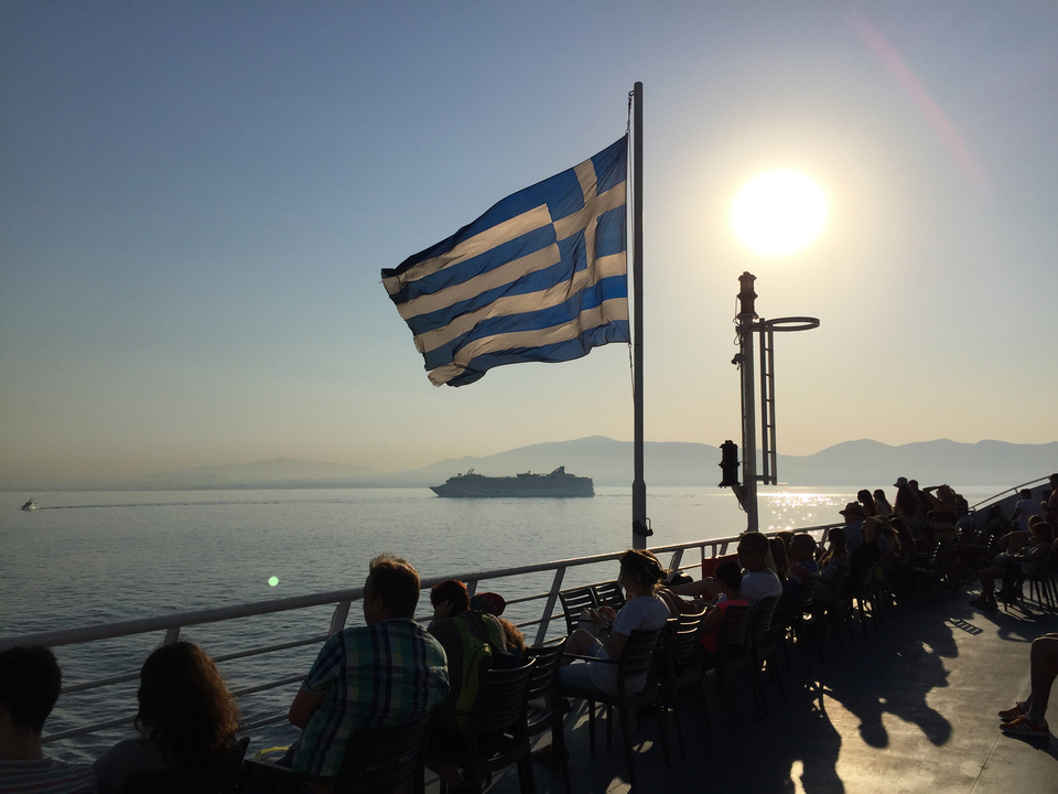 Greek flag waving on a ferry with passengers enjoying the sea view.