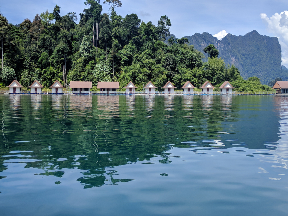 Floating bungalows on a lake with mountains in the background.