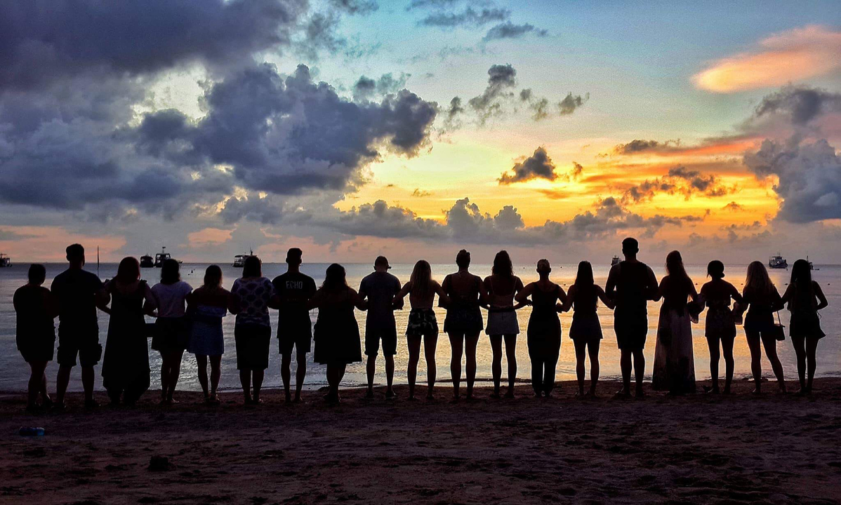 Silhouette of a group of people holding hands on a beach at sunset.