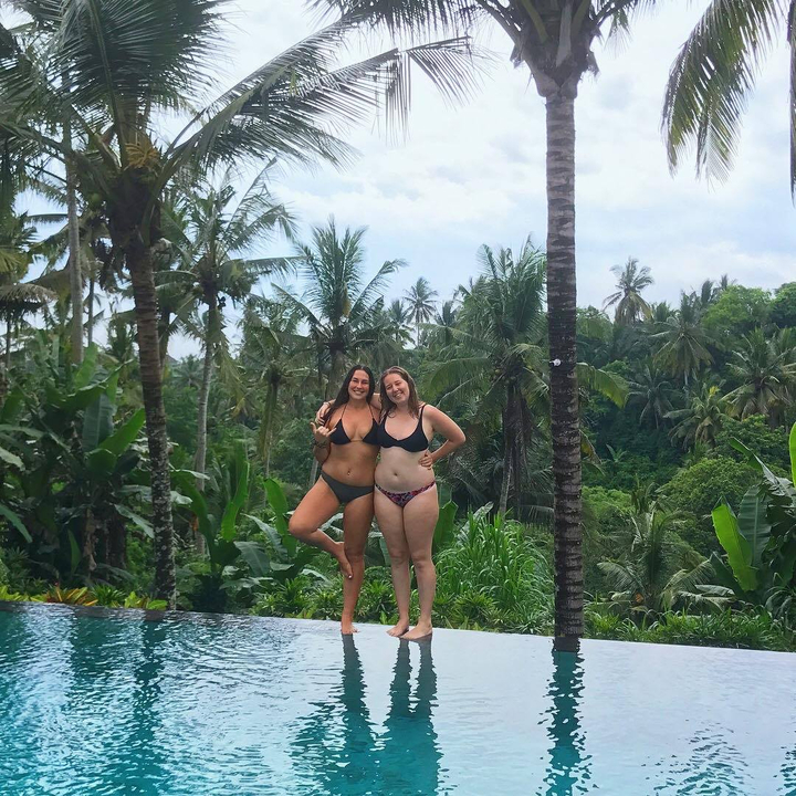 Two women posing in swimsuits with a tropical forest background.