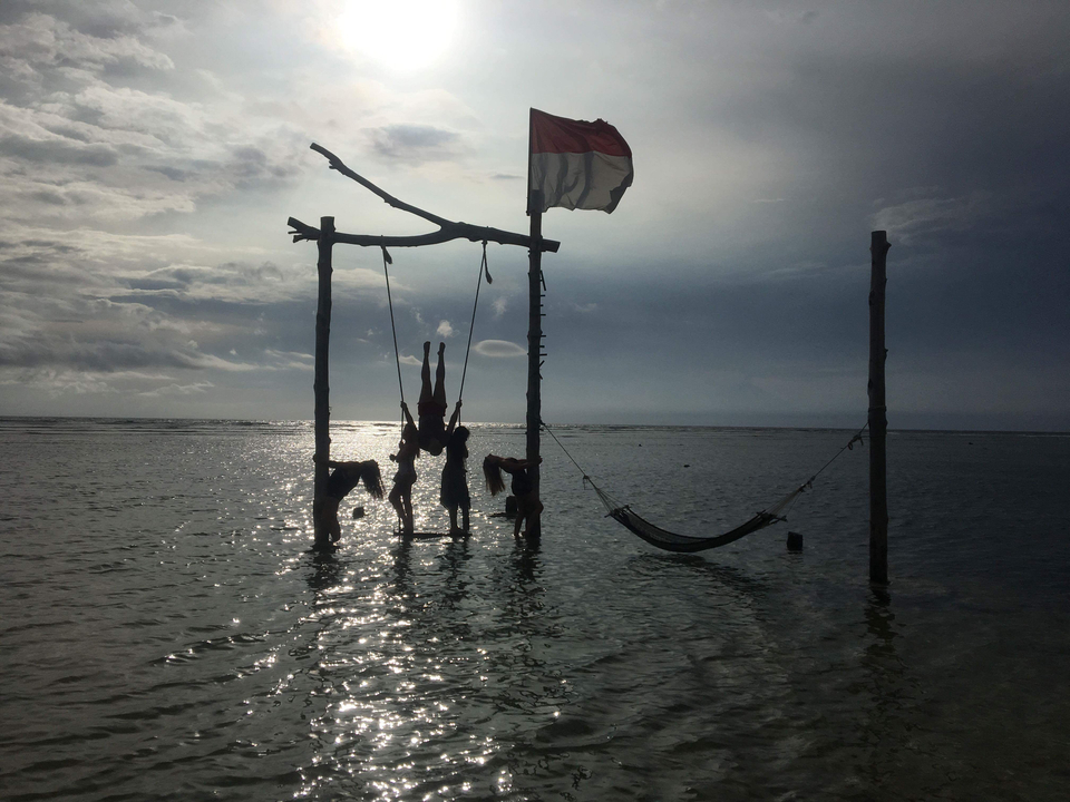 Group playing on a swing set in the water with a flag in the background.