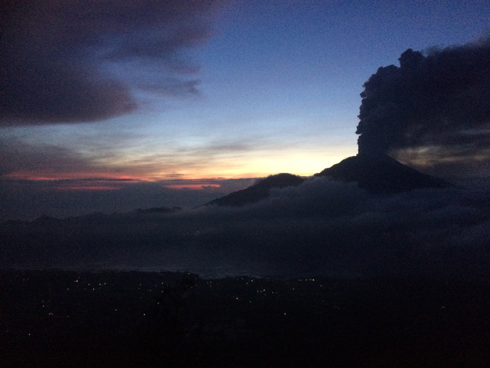 Volcanic mountain during sunset with dark clouds and lights below.
